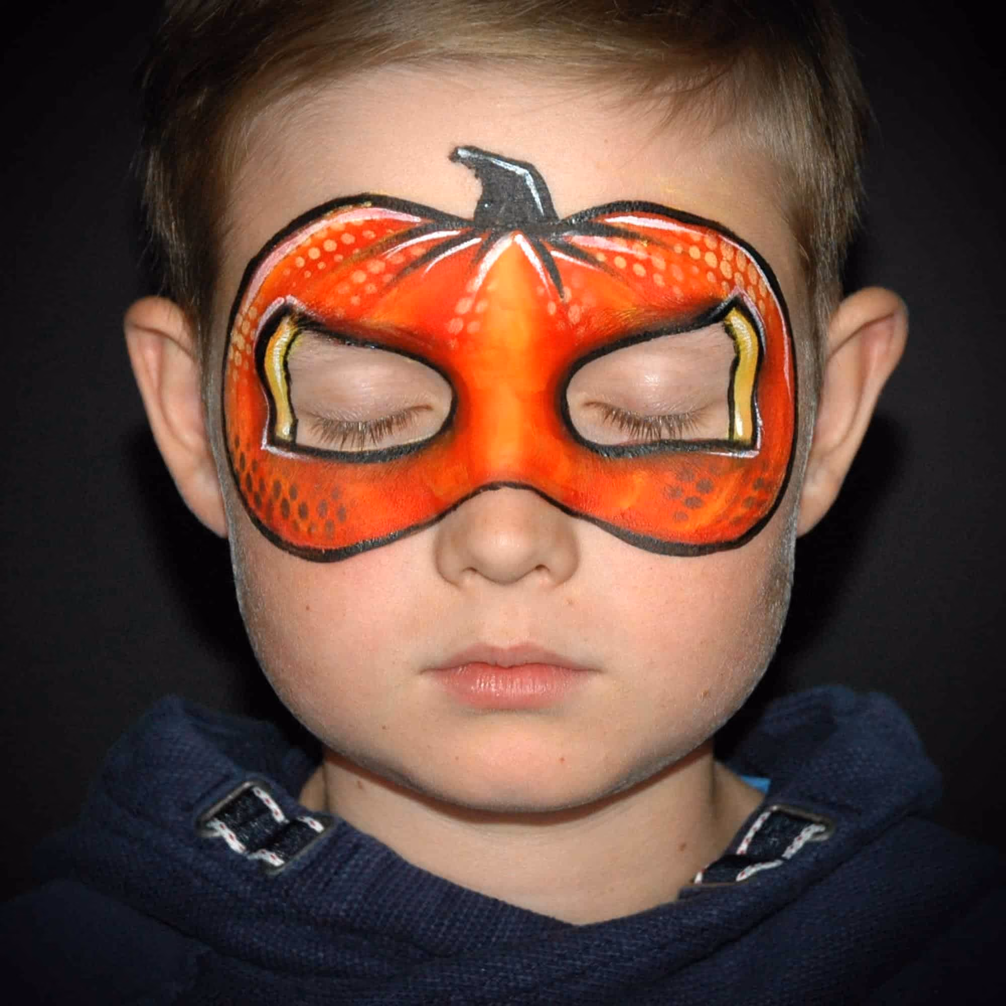 a boy with an shaded orange pumpkin face paint around his eyes