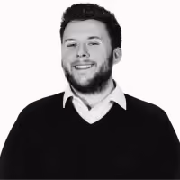 Smiling man with beard wearing a black sweater over a white collared shirt against a white background.