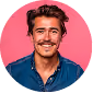 Smiling young man with a mustache and styled hair wearing a blue shirt against a pink background.