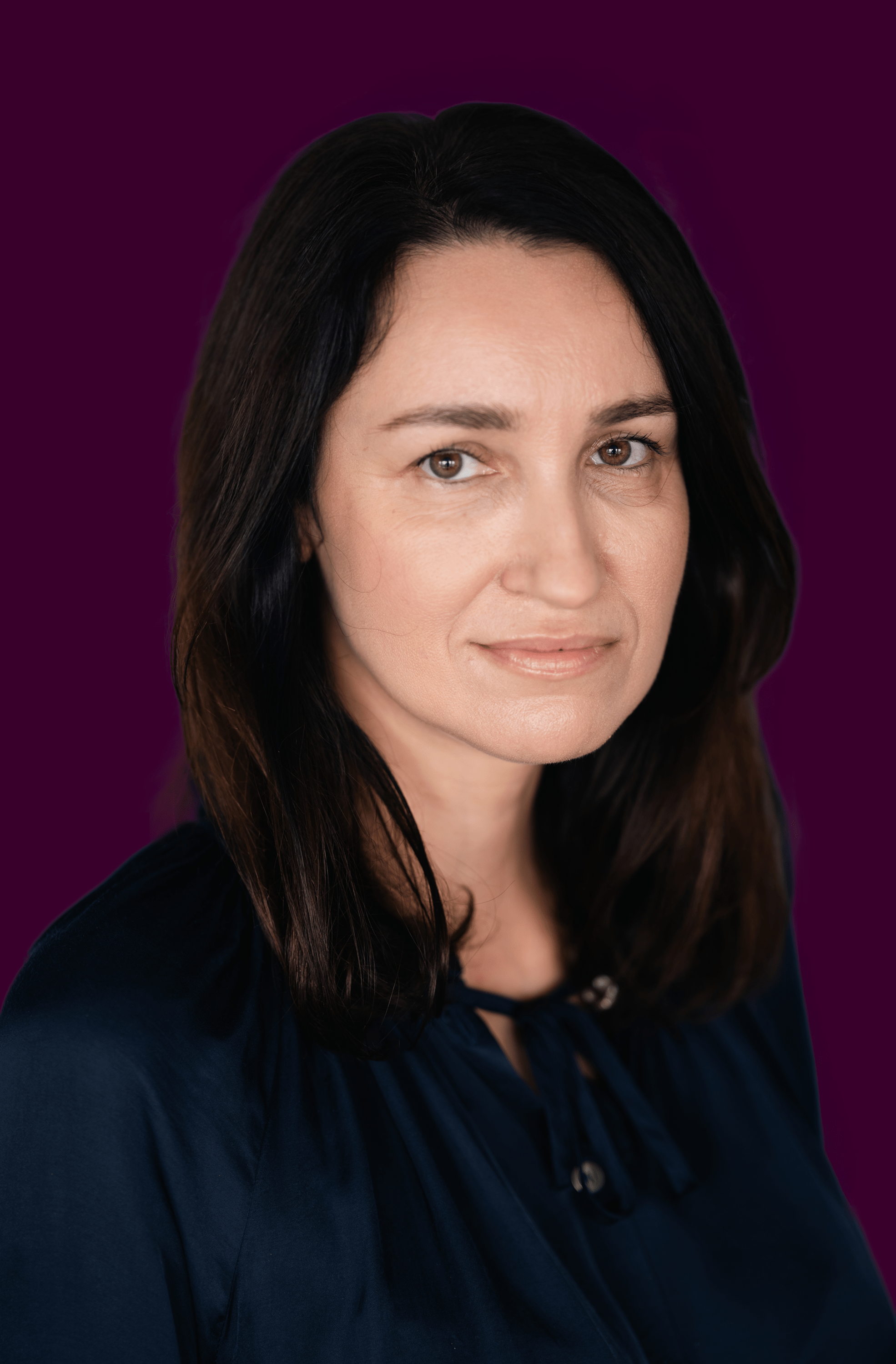 Portrait of a woman with dark hair wearing a navy blouse against a dark purple background.