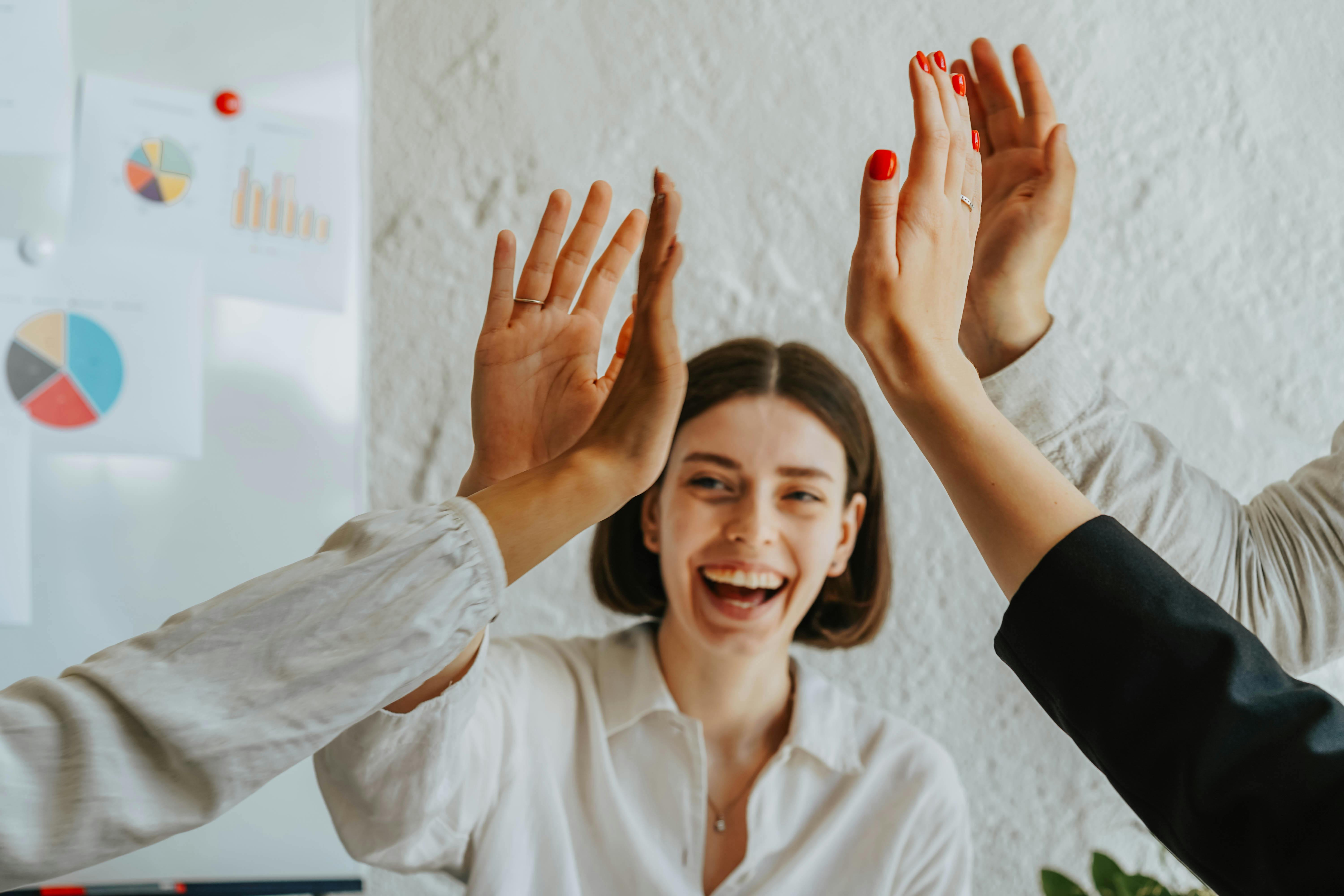 Smiling young woman and colleagues giving a group high five in an office setting.