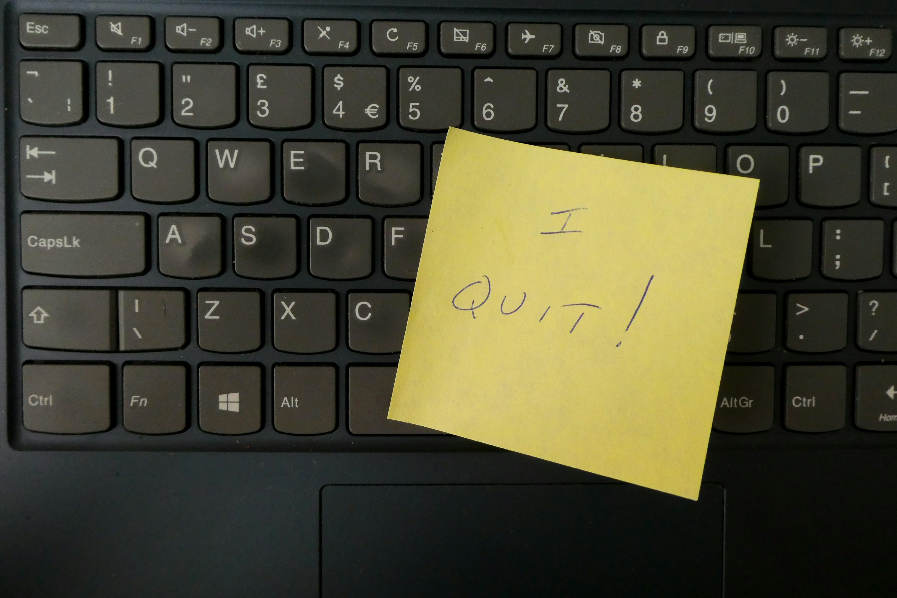 Black laptop keyboard with a yellow sticky note displaying handwritten text 'I QUIT!'