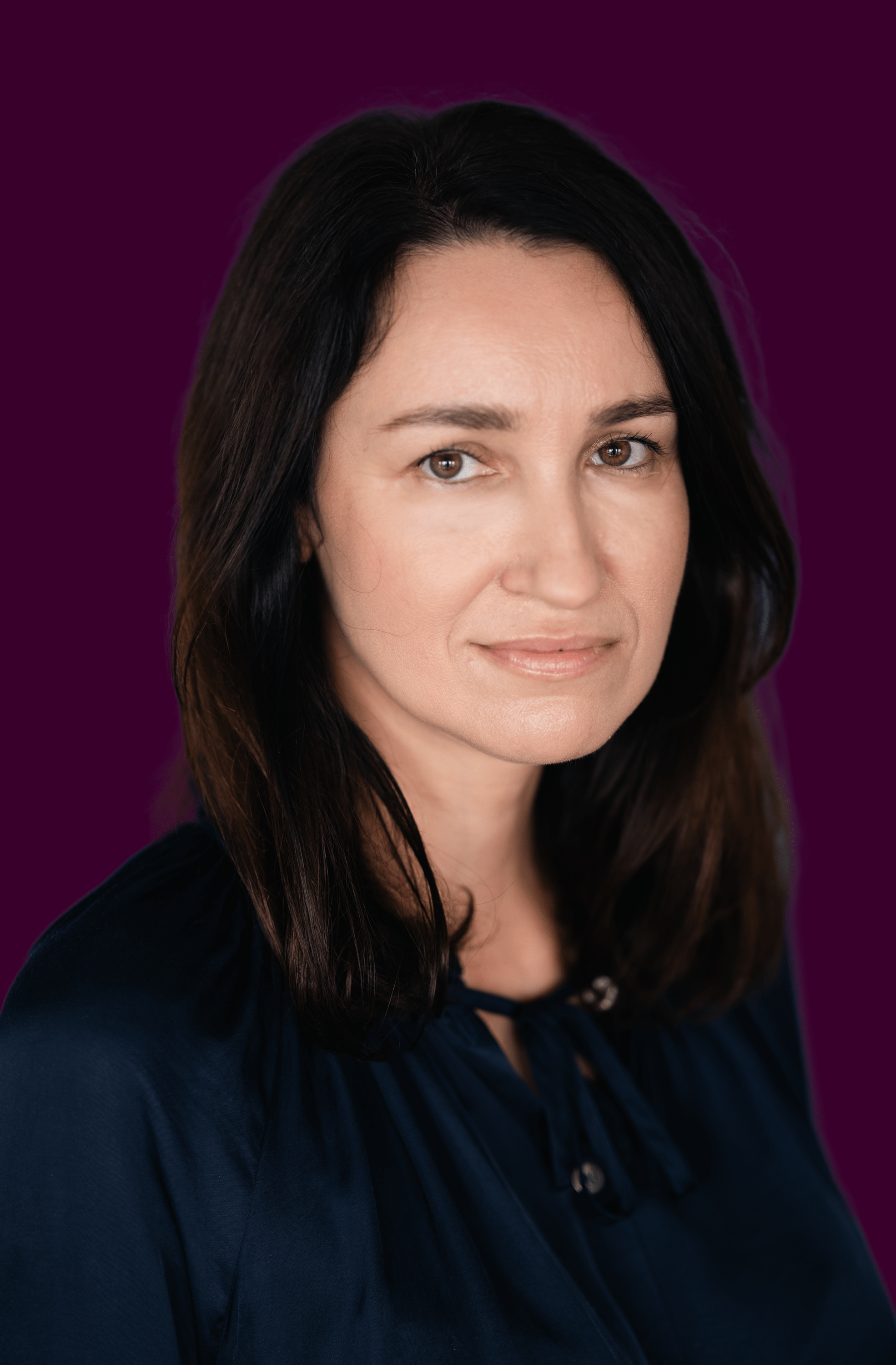 Woman with shoulder-length dark hair wearing a dark blue blouse against a deep purple background.