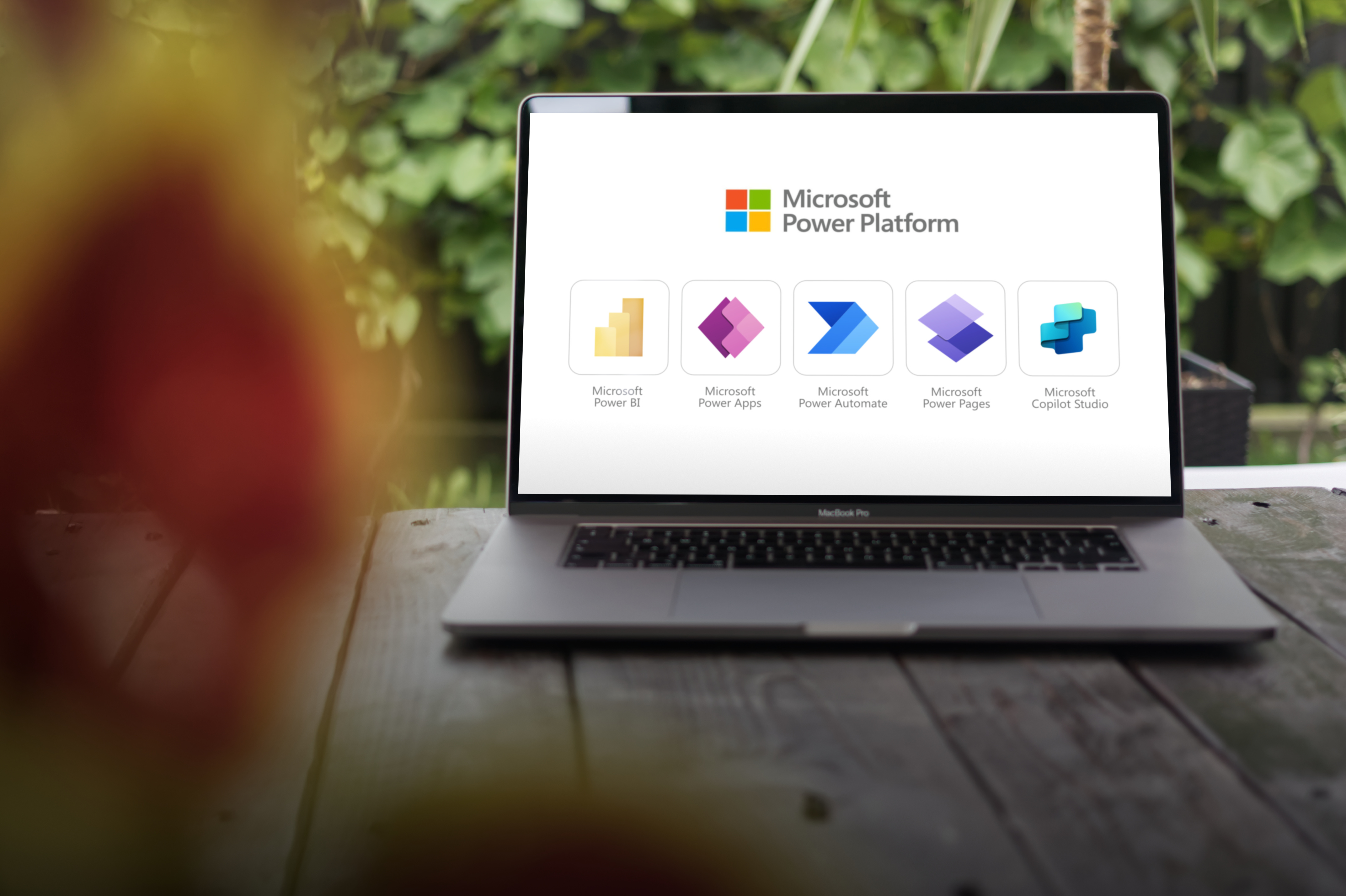 Open laptop on wooden table displaying Microsoft Power Platform icons for Power BI, Power Apps, Power Automate, Power Pages, and Copilot Studio.