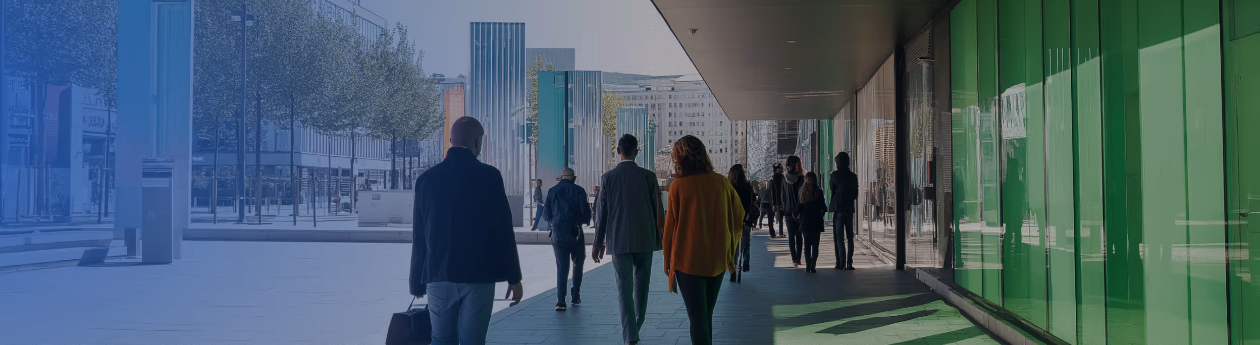 People walking in a modern corridor - A panoramic view of several people walking down a bright, modern corridor with glass walls and green accents, suggesting a public space like an airport or convention center. 