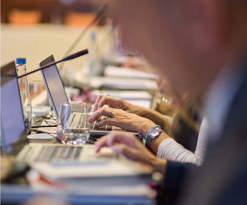 People typing on laptops in an office setting - Close-up view of hands typing on laptop keyboards in a professional environment, showing a busy work atmosphere with multiple computers in use.