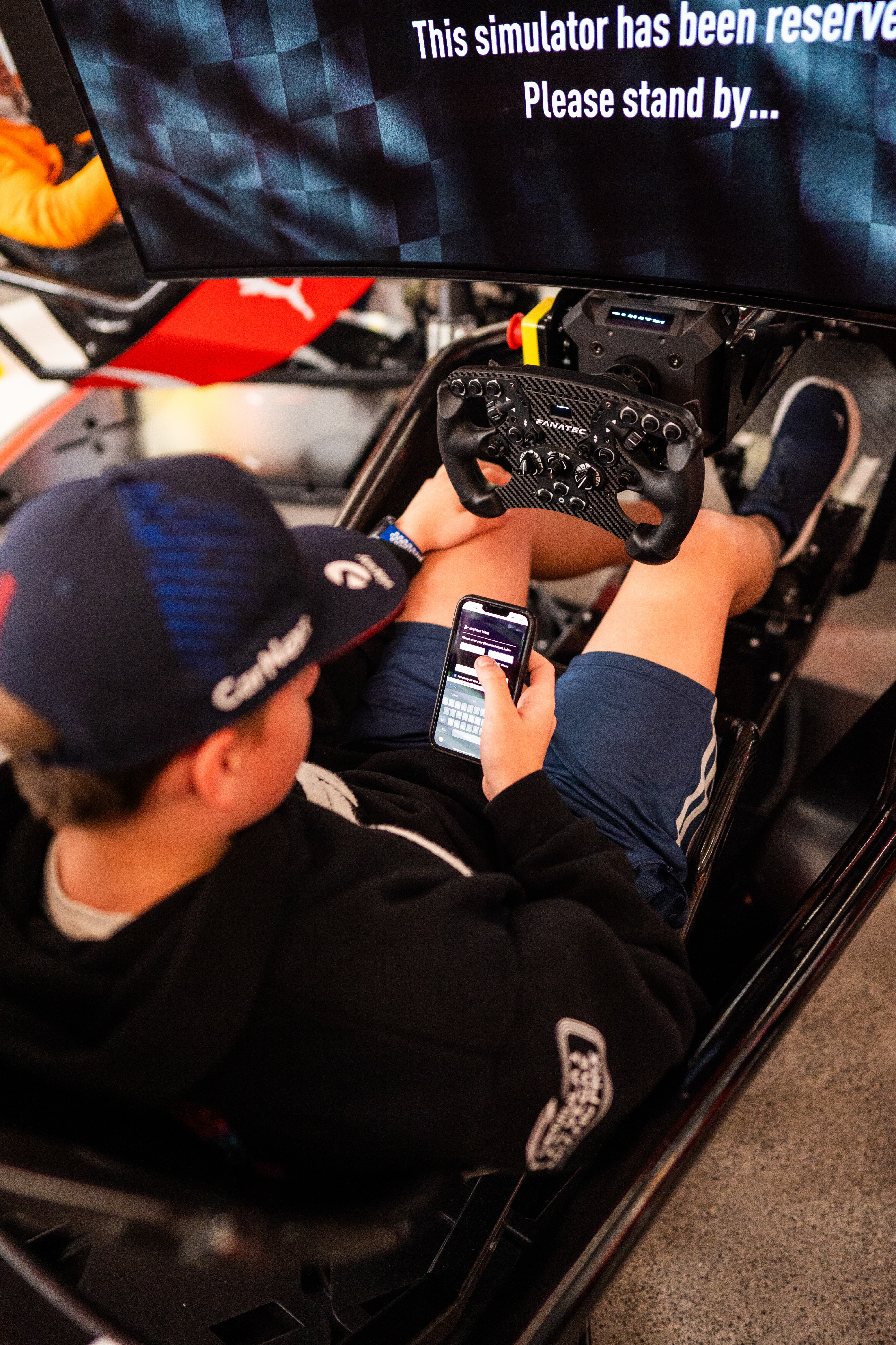 Person sitting in a racing simulator holding a phone with a reserved simulator message on the screen.