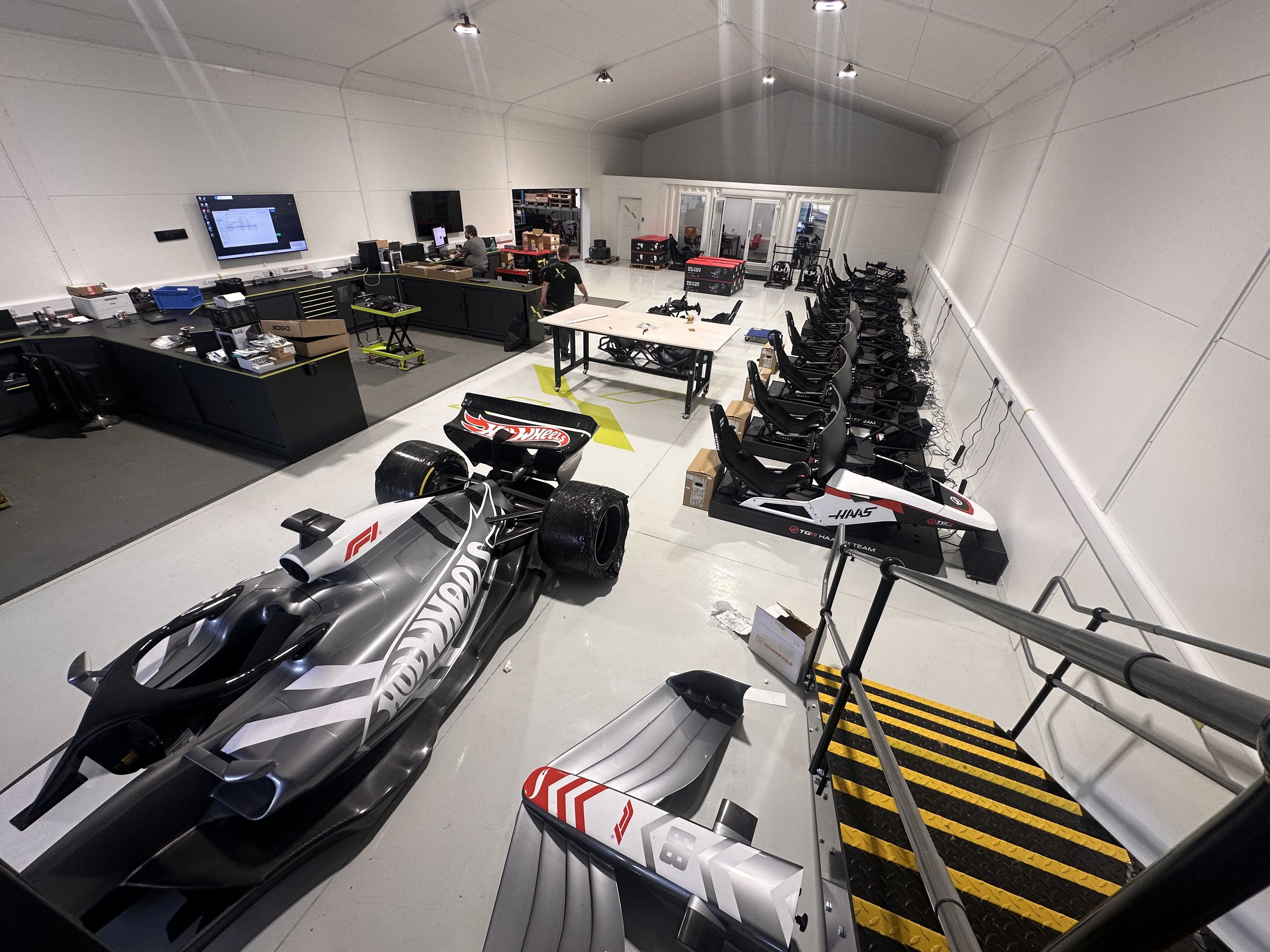 Indoor space with a race car and multiple racing simulator setups lined up along a wall.