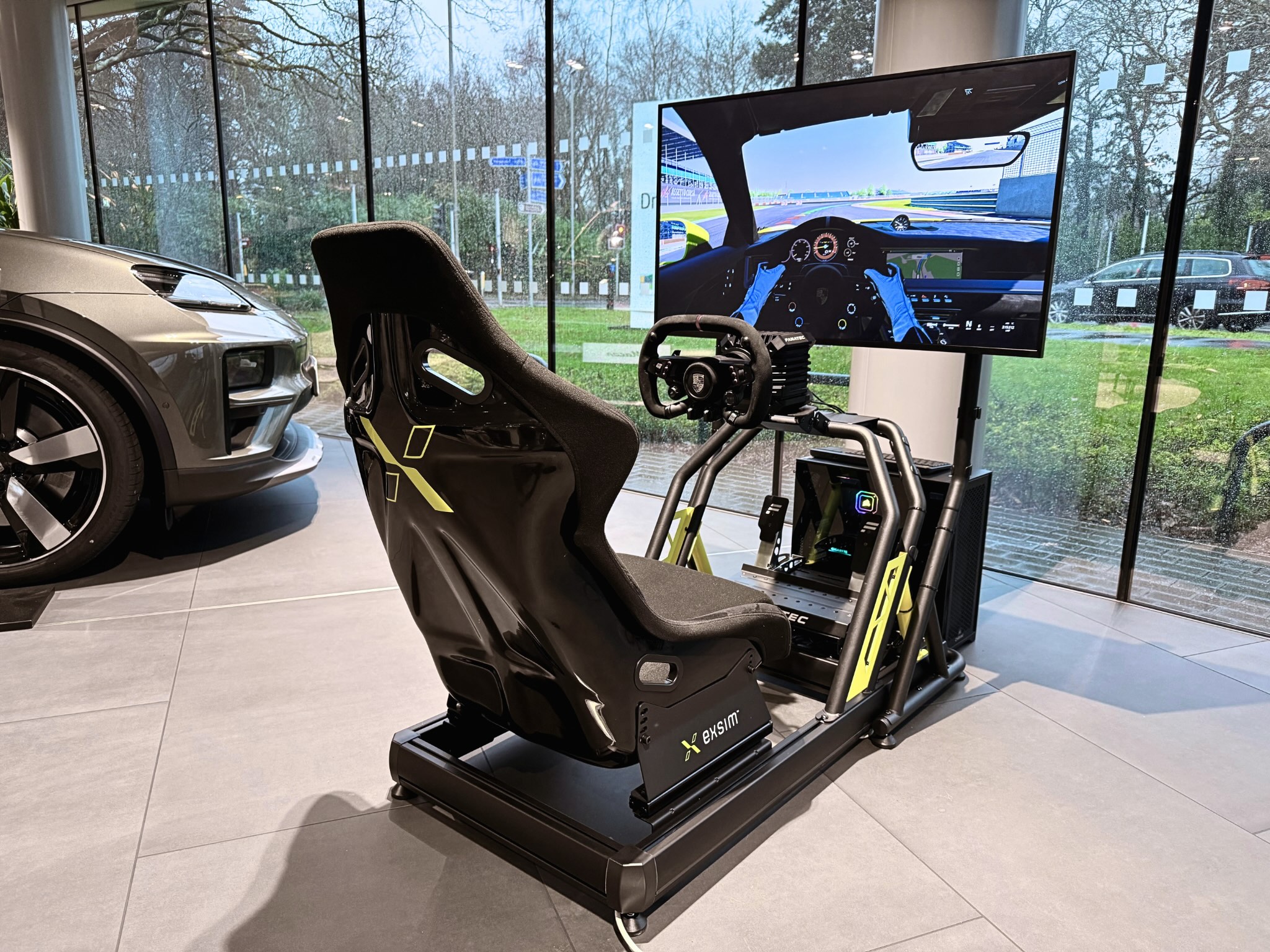 Racing simulator setup with a seat, steering wheel, pedals, and a monitor showing a car racing game.