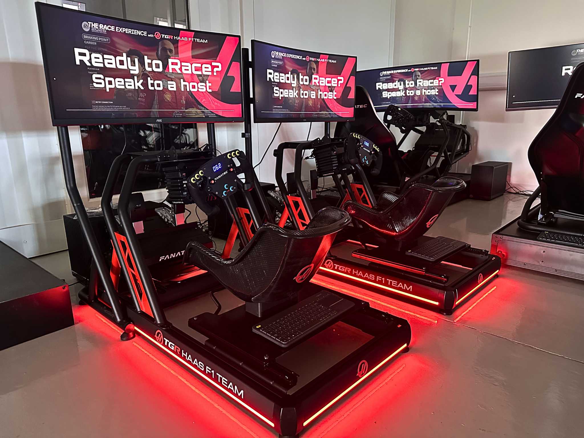 Two TGR Haas F1 Team racing simulators with screens showing 'Ready to Race? Speak to a host.'