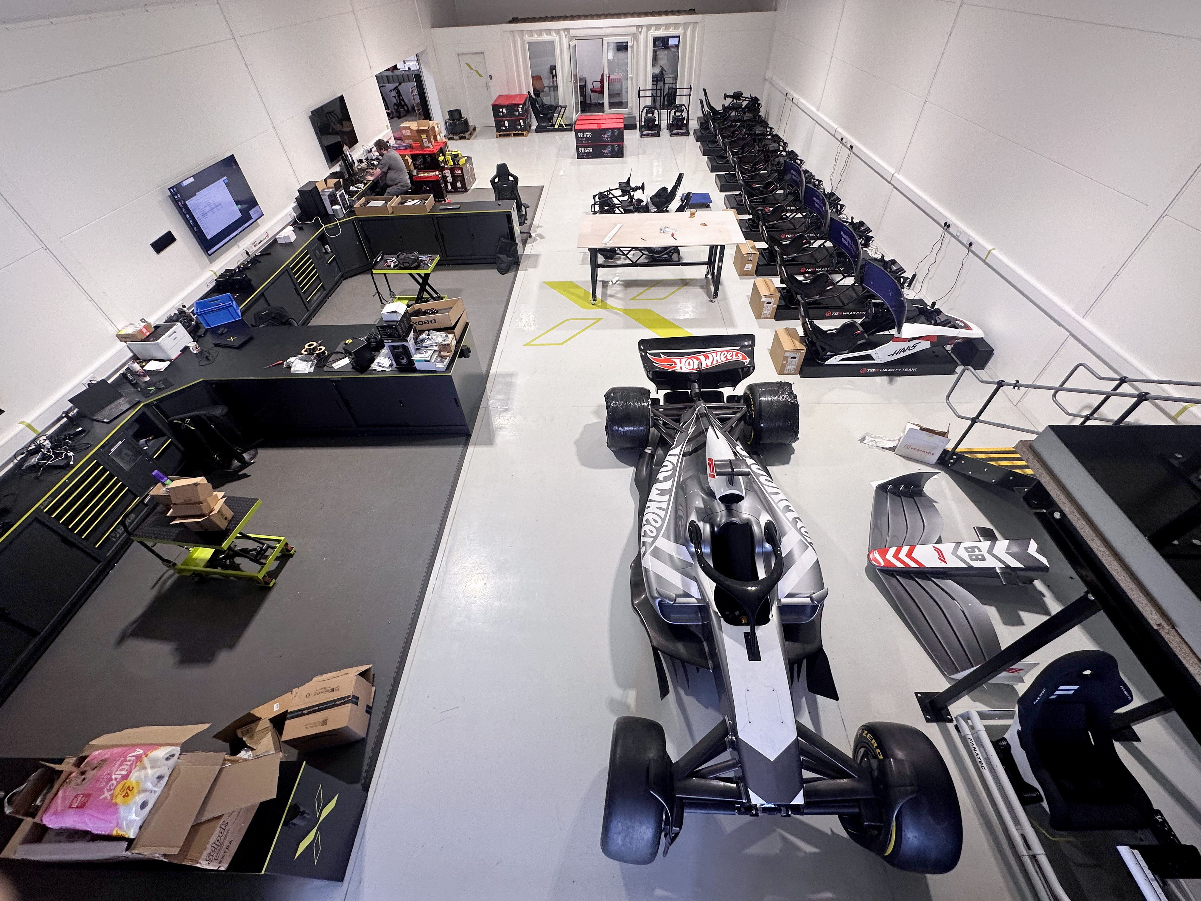 Man kneeling assembling a white Formula 1 racing simulator cockpit with Fanatec steering wheel base.