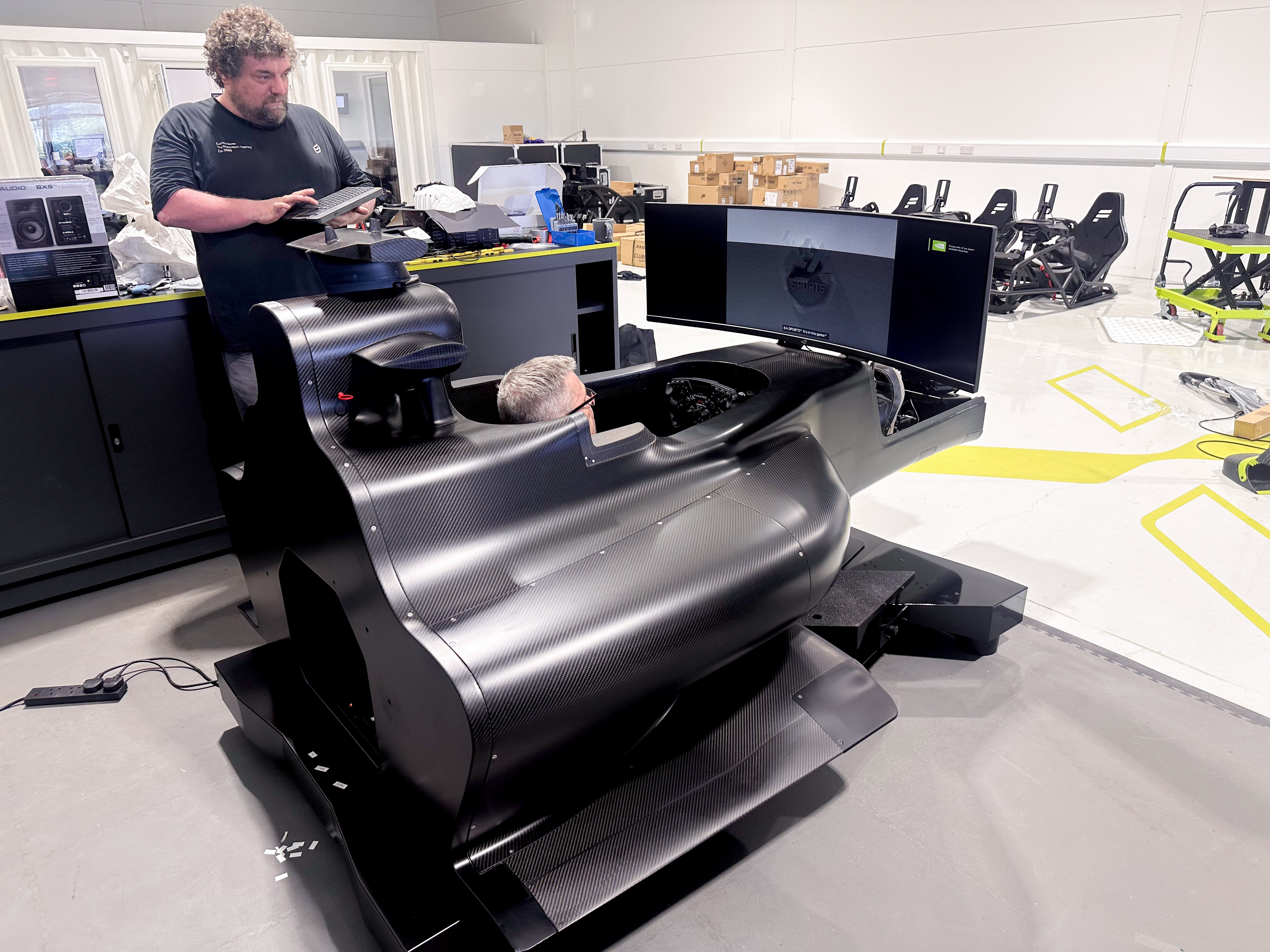 Row of black racing simulator seats each with a steering wheel and large screen labeled GT SIM 1 to 5.