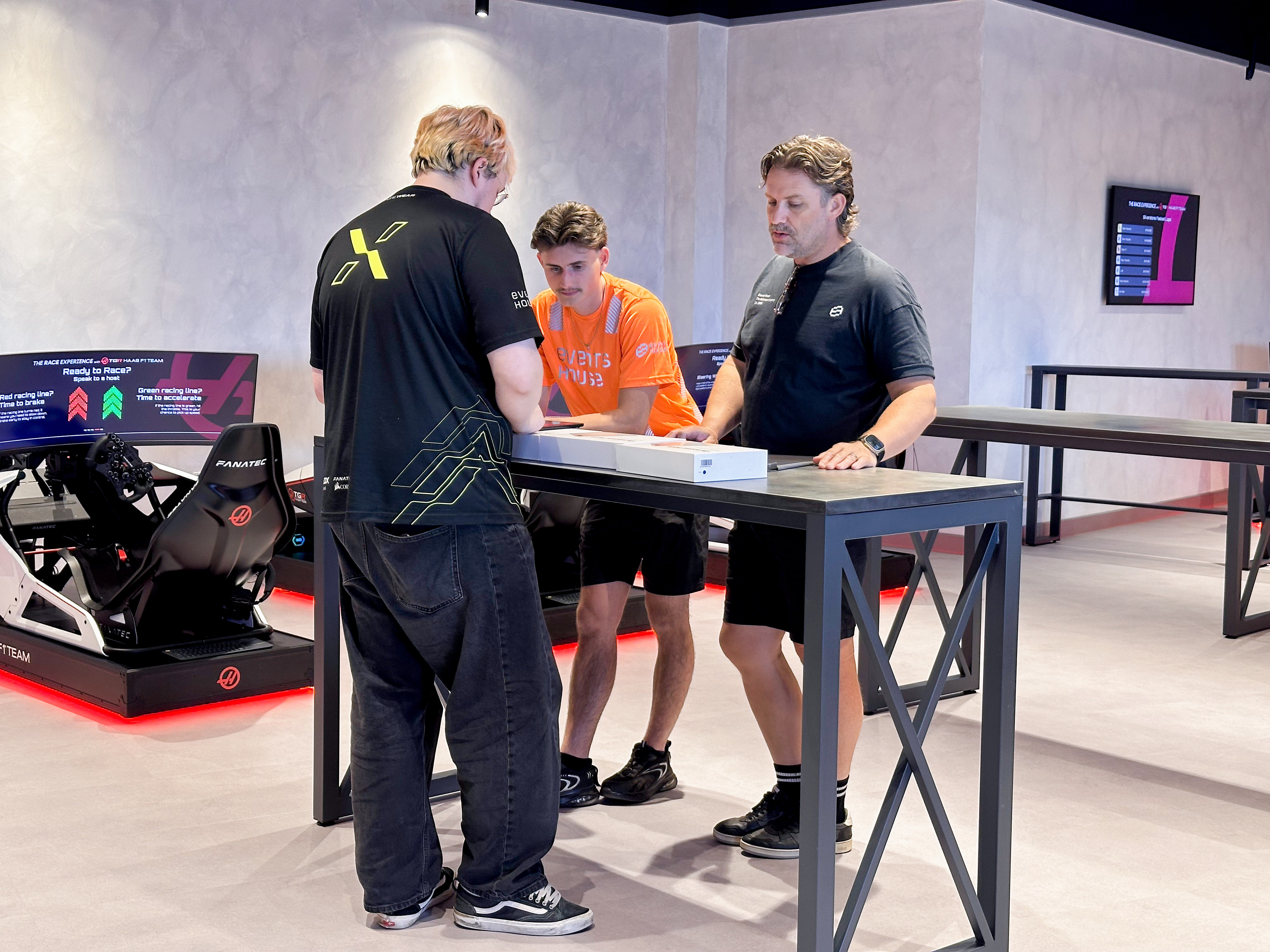 Indoor space with a race car and multiple racing simulator setups lined up along a wall.