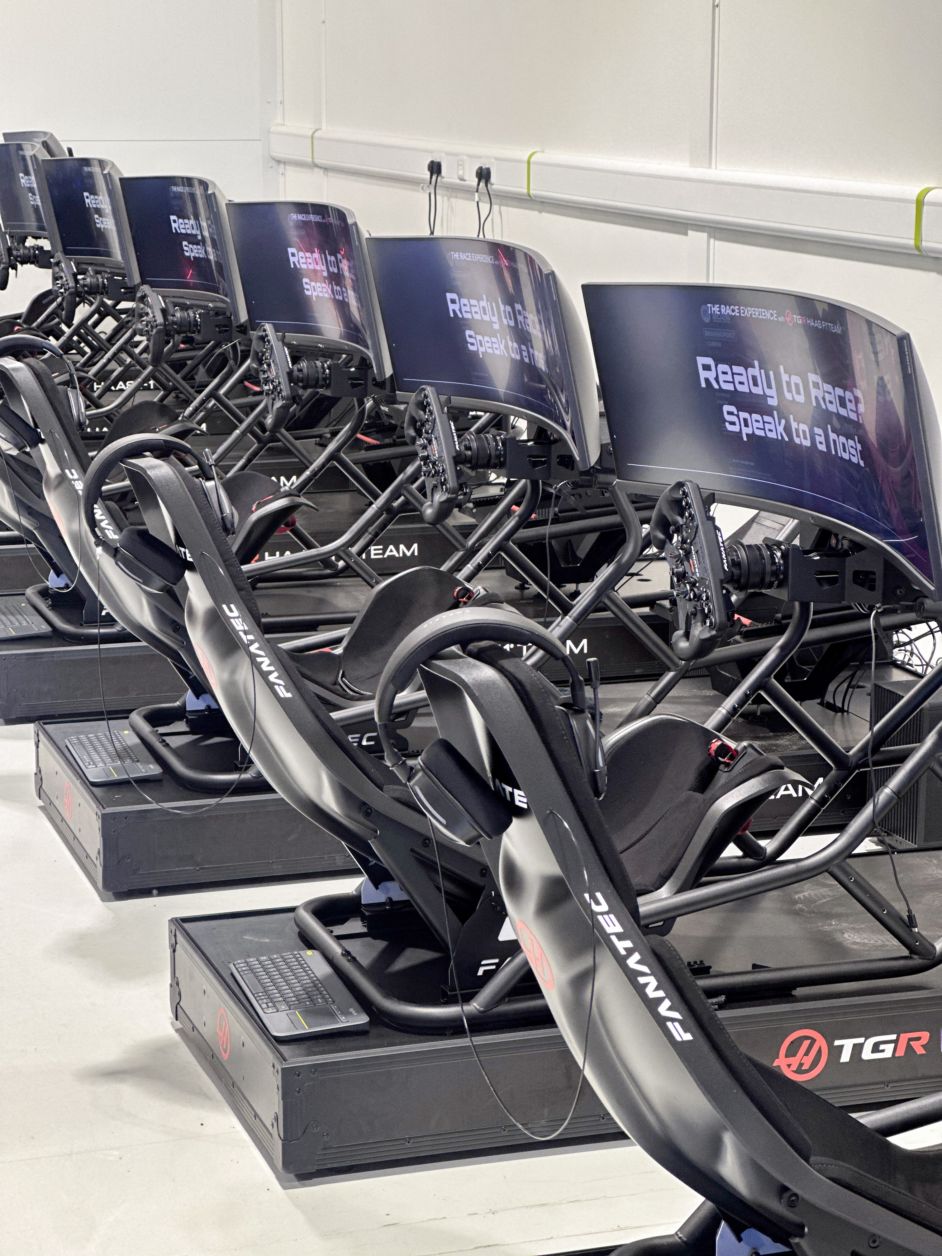 Man kneeling and working on a Mercedes F1 racing simulator in a large indoor space.
