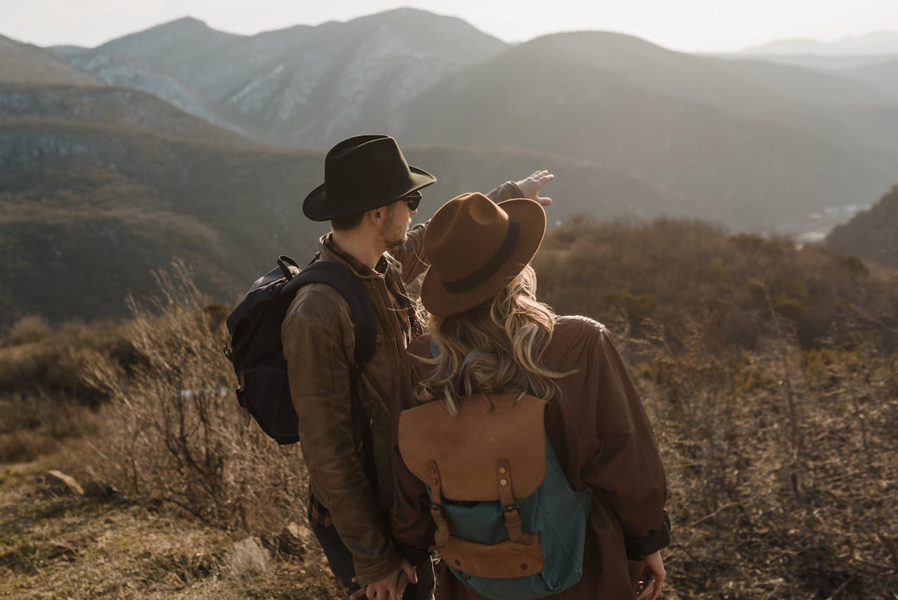Couple de randonneurs en chapeaux, vus de dos, admirant un vaste paysage montagneux au loin.