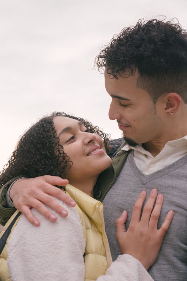 Gros plan sur un jeune couple s'observant avec tendresse et complicité, l'homme serrant la femme dans ses bras.