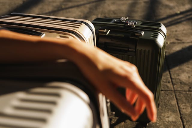 Gros plan sur deux valises modernes de voyage, avec une main posée sur l'une d'elles, sous la lumière du soleil.
