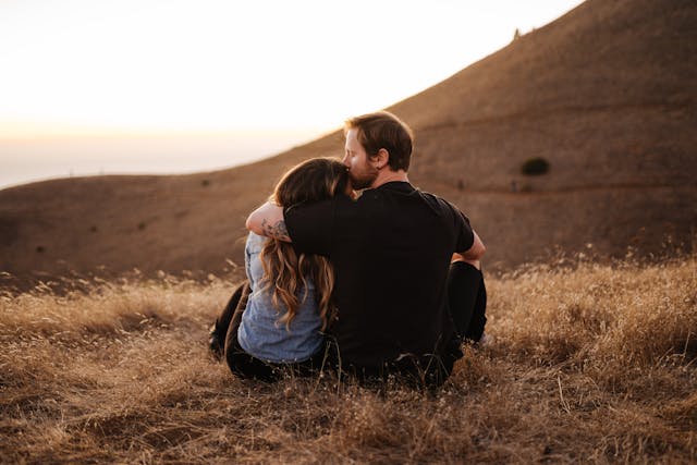 Couple s'enlaçant tendrement sur une colline couverte d'herbes sèches, admirant le coucher du soleil