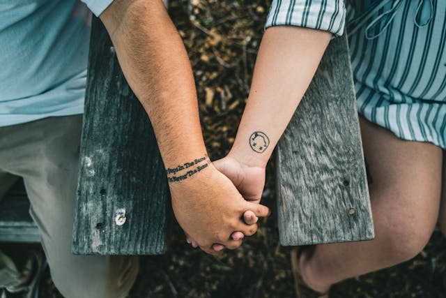 Gros plan sur les mains tatouées d'un couple se tenant mutuellement, posées sur un banc en bois.
