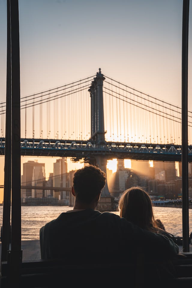 Couple vu de dos sur un banc, regardant le pont de Manhattan et la skyline de New York au coucher du soleil