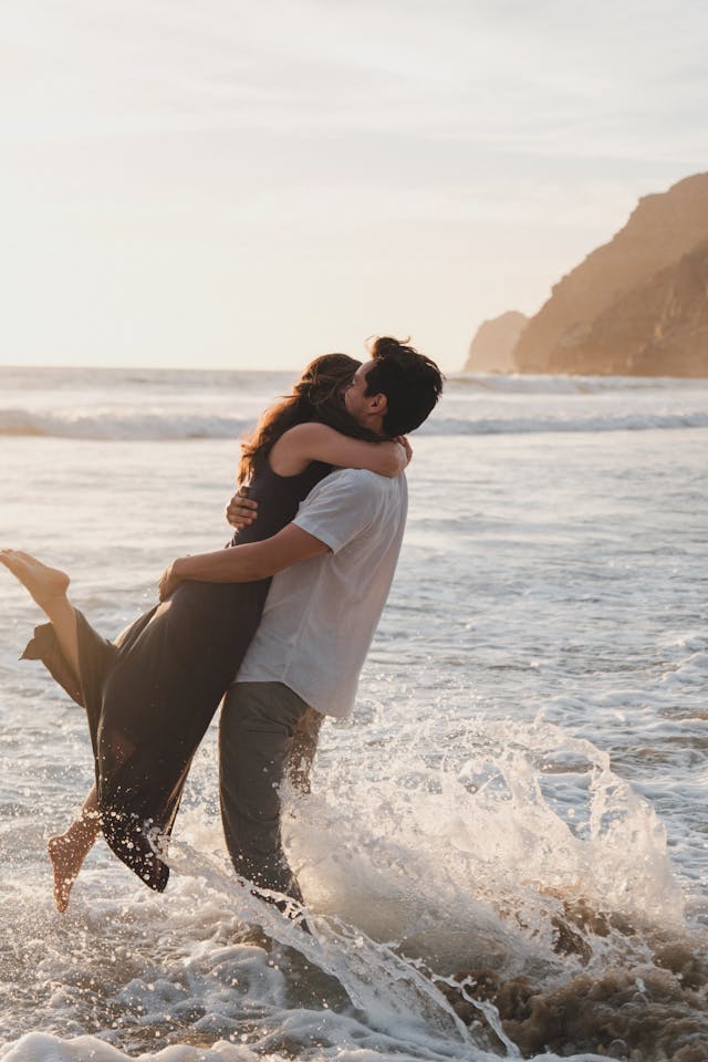 Couple s'embrassant et jouant dans les vagues sur une plage au coucher du soleil.