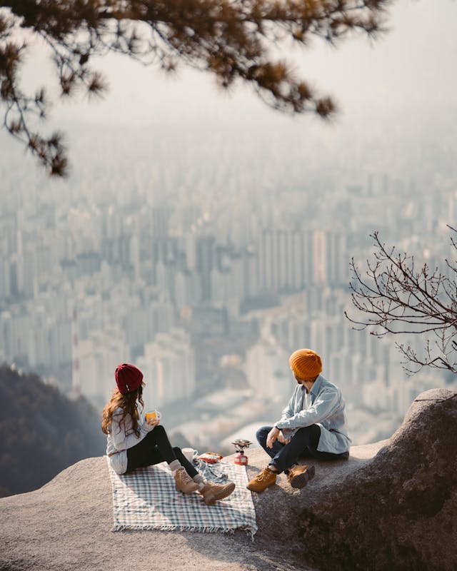Couple pique-niquant sur une montagne avec une vue panoramique sur la ville en contrebas.
