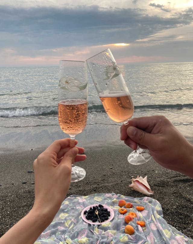 Deux verres de vin rosé portés sur une plage au coucher du soleil, ambiance romantique