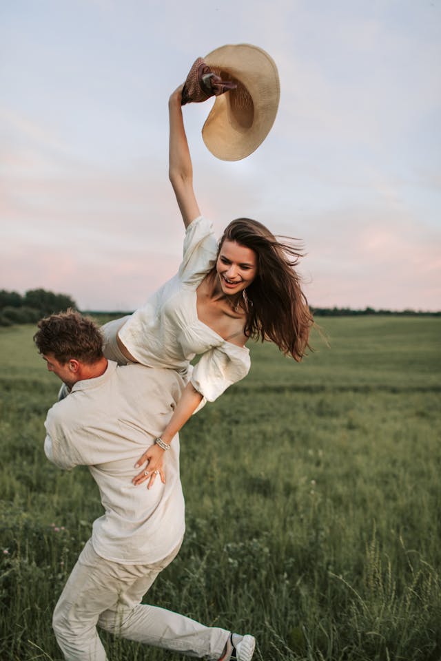 Couple joyeux s'amusant dans un champ verdoyant au coucher du soleil, ambiance estivale.