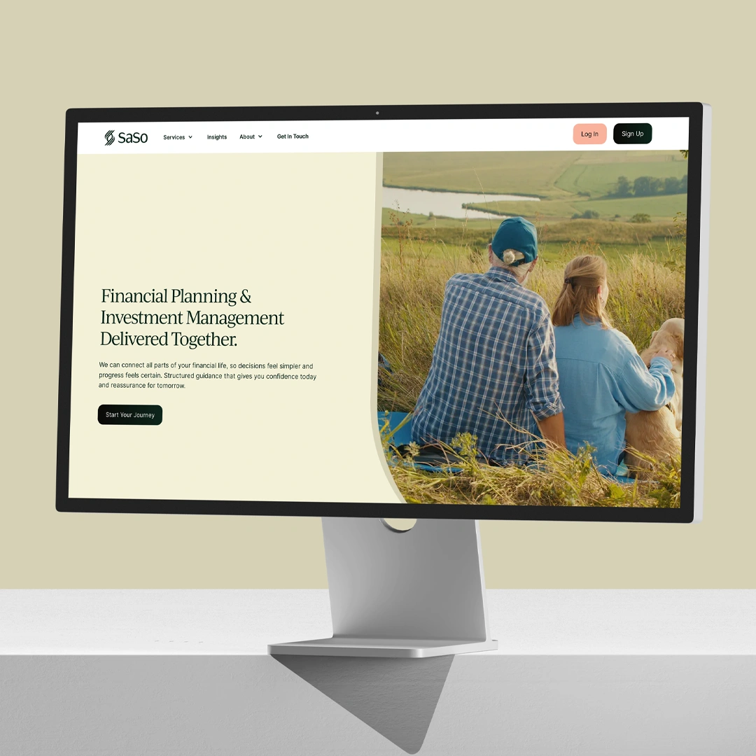 Computer screen displaying SaSo website homepage with financial planning and investment management message alongside an image of two people sitting in a grassy field with a golden retriever dog, overlooking a scenic landscape with a river.