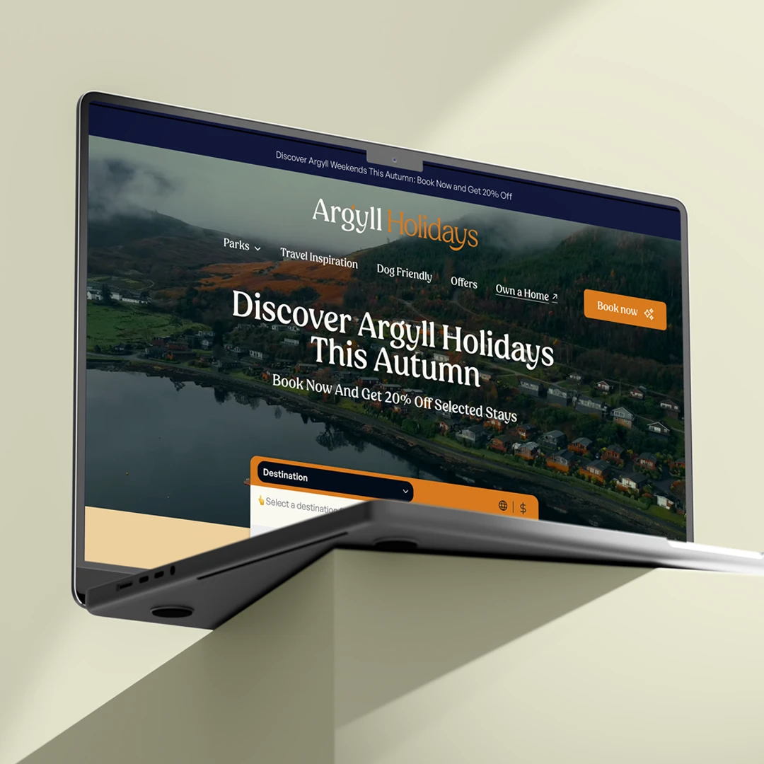 Laptop displaying Argyll Holidays website homepage with an autumn landscape of hills, houses by a lake, and navigation options including Parks, Travel Inspiration, Dog Friendly, Offers, and Own a Home, with a Book Now button.