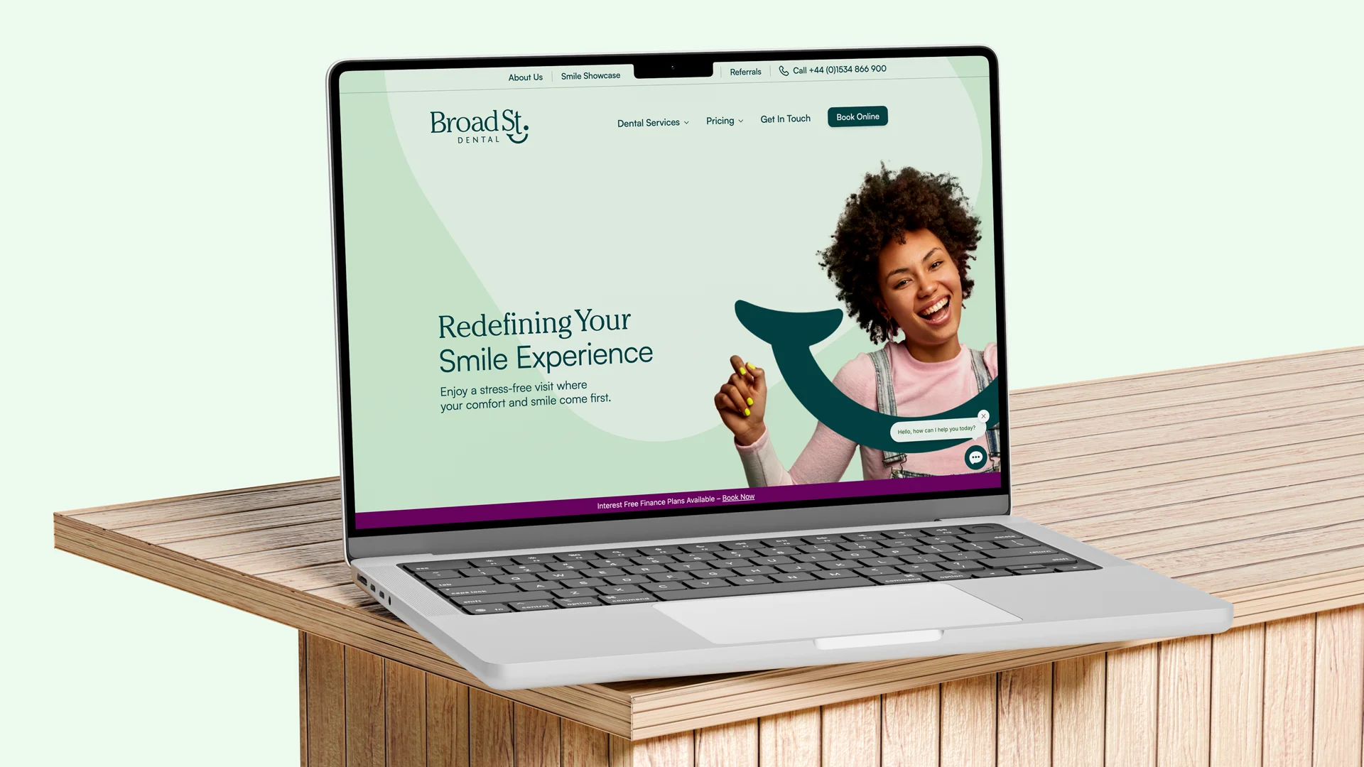 Laptop on a wooden table showing Broad St Dental website with a smiling woman and text 'Redefining Your Smile Experience' and options for dental services, pricing, and booking online.