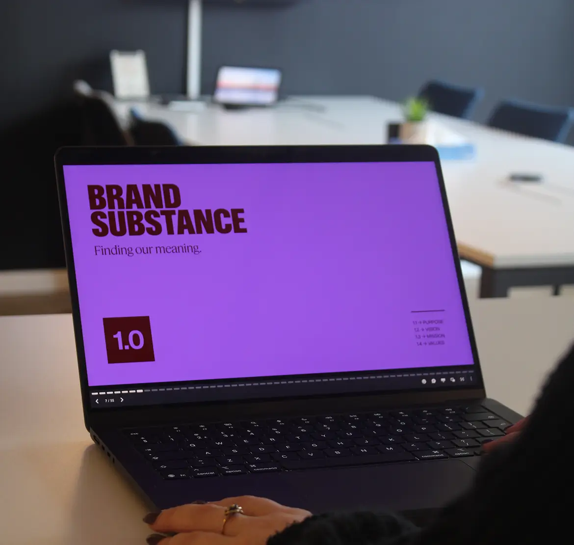 Laptop screen displaying a purple slide titled 'BRAND SUBSTANCE' with the subtitle 'Finding our meaning.' A small red box shows '1.0' on the slide, which appears to be part of a presentation in a conference room setting.