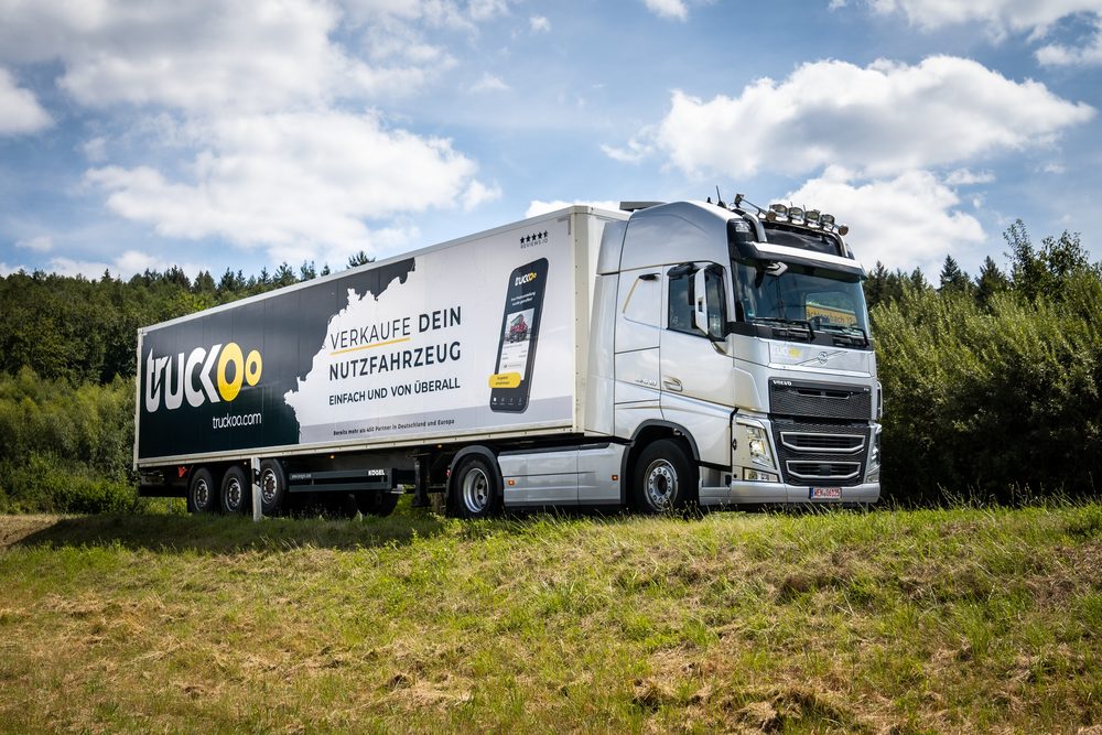truckoo Sattelzug mit Werbebeklebung auf einer Wiese, Seitenansicht