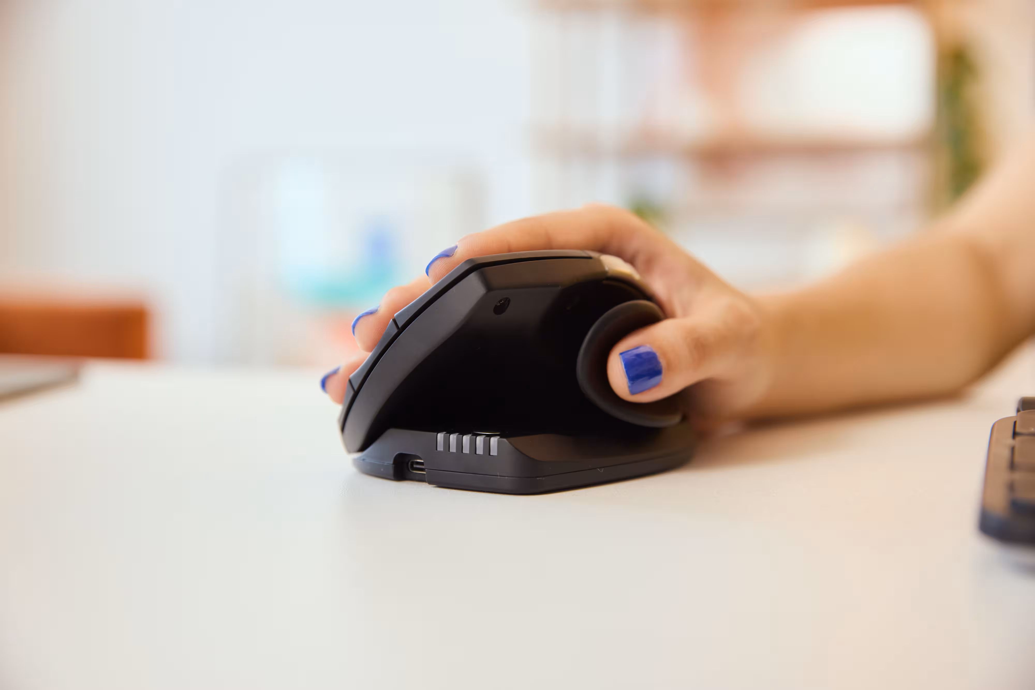 Hand using the Contour Unimouse in a neutral, vertical grip position on a desk, demonstrating ergonomic design that reduces strain on the wrist and thumb