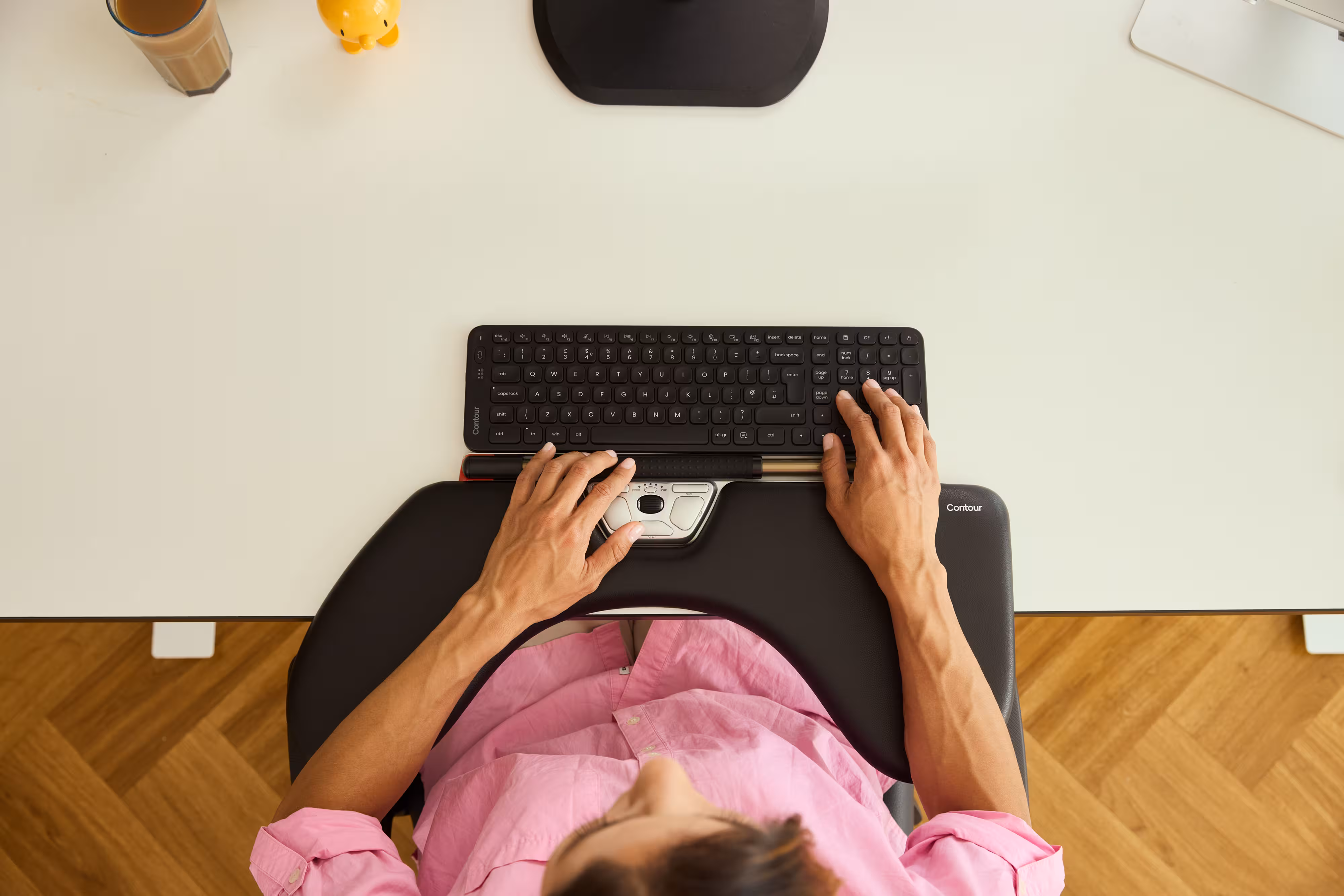 Top-down view of a person typing on a keyboard while using a Contour RollerMouse. Their hands rest on the built-in wrist support, showing a centered, ergonomic workstation setup.