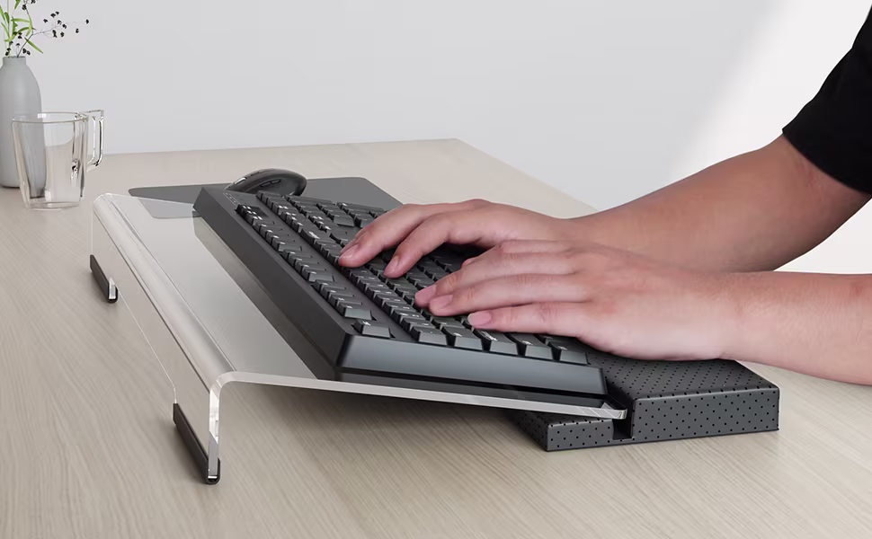 Person typing on a keyboard placed on an elevated ergonomic keyboard riser with a wrist rest, demonstrating raised and angled positioning for neutral wrist posture.