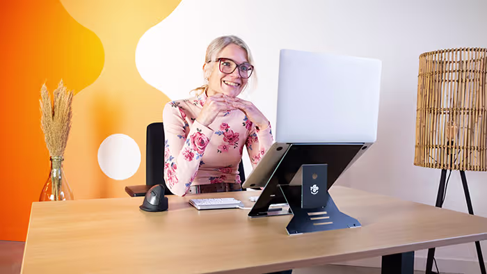Woman with glasses using an adjustable laptop stand at optimal viewing angle on desk.