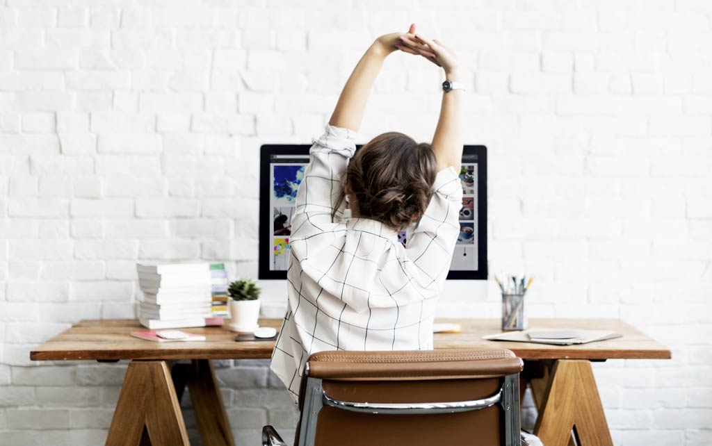 Woman performing wrist isometric hold for mouse elbow at a home desk.