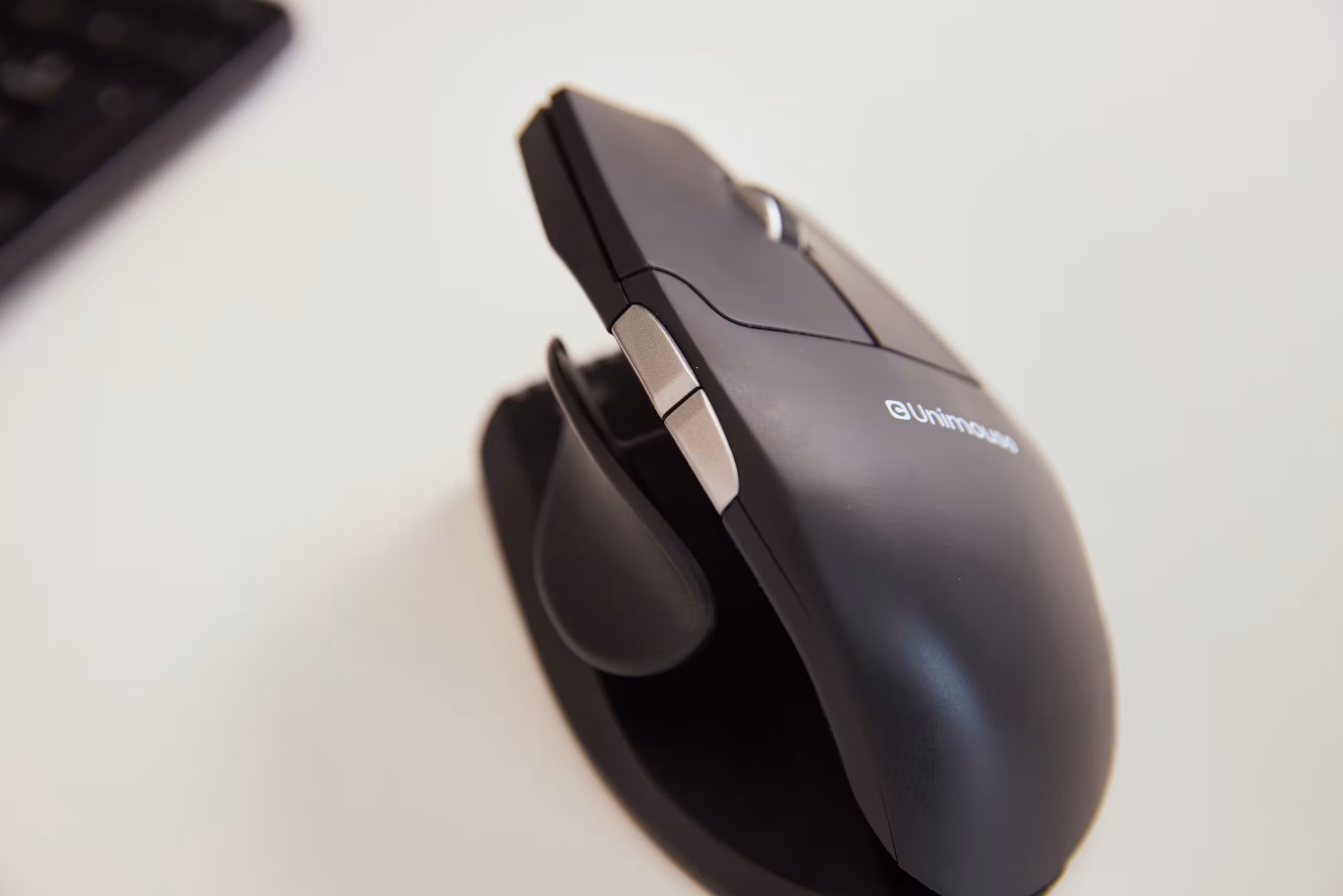 Close-up of a black Contour Design Unimouse ergonomic vertical mouse with adjustable thumb support, shown on a white desk.