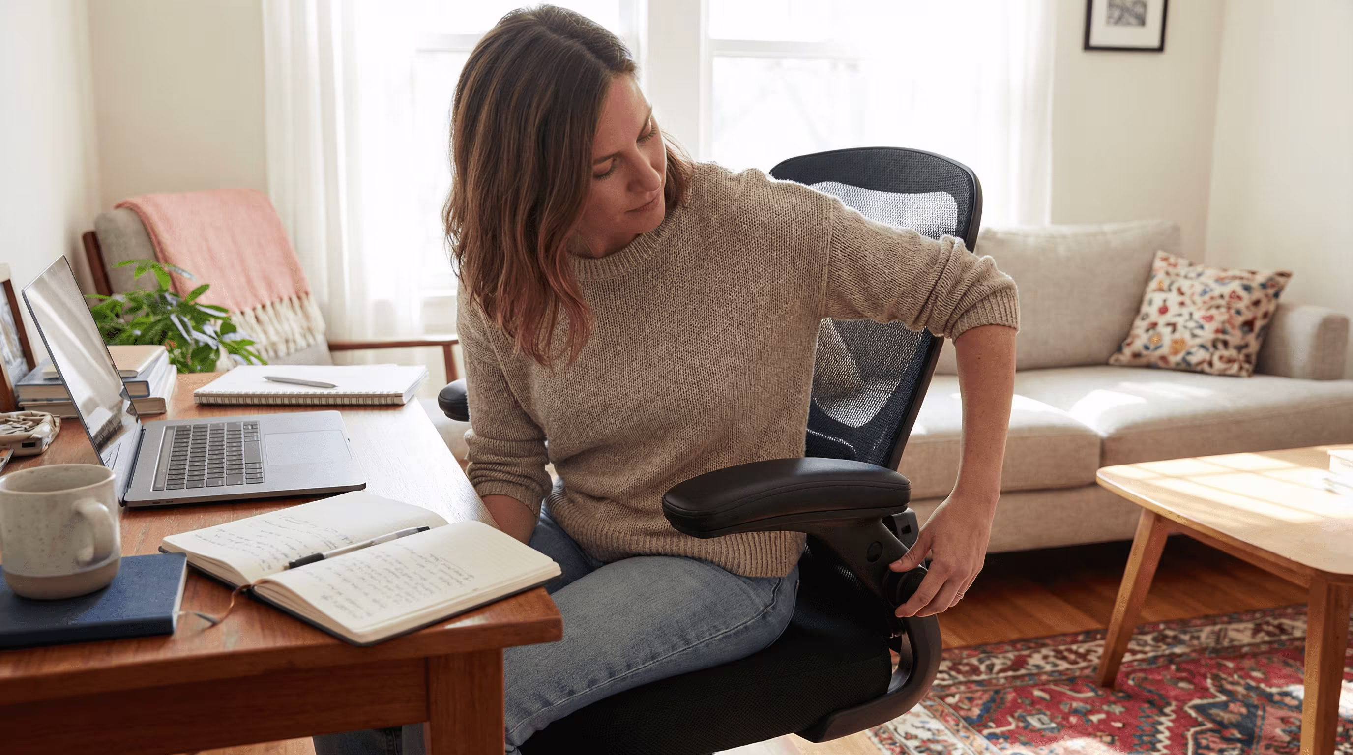 Woman adjusts armrest for neutral elbow support at a home desk.