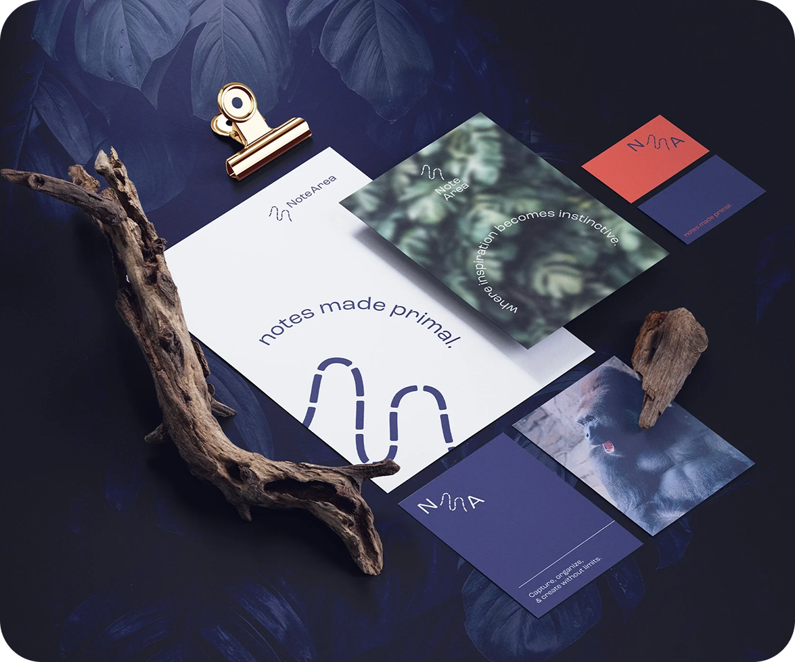 Flat lay of Note Area branded stationery including cards and paper with leaf patterns, wood pieces, and a gold clip on a dark blue background.