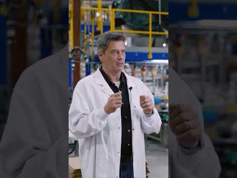 Carl Tokarek of Maneva, in a white lab coat, speaks about worker safety on a factory floor.