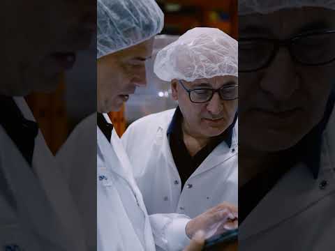 A worker in a hairnet and glasses checks a production line.