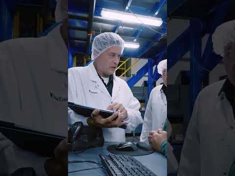 Two workers in hairnets and white coats review a tablet on a food production floor.