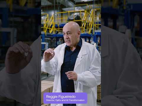 Reggie Figueiredo of Maneva, in a white lab coat, speaks on a factory floor.