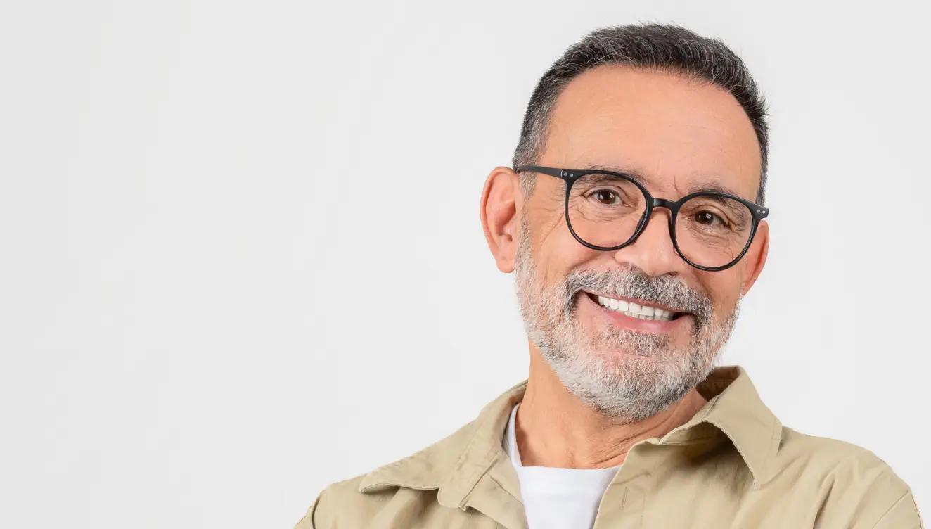 A person with glasses smiles warmly, wearing a beige shirt, against a plain background.