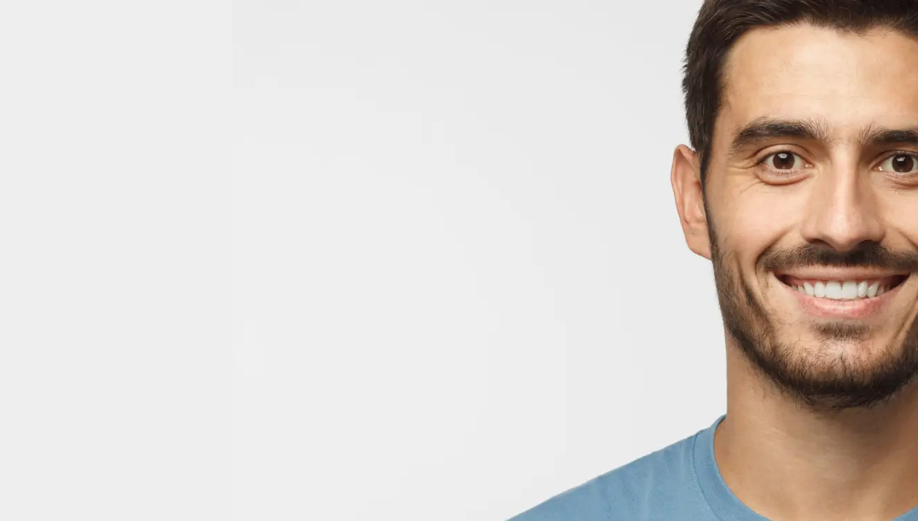 A man with short dark hair and a beard is smiling at the camera, wearing a blue shirt.