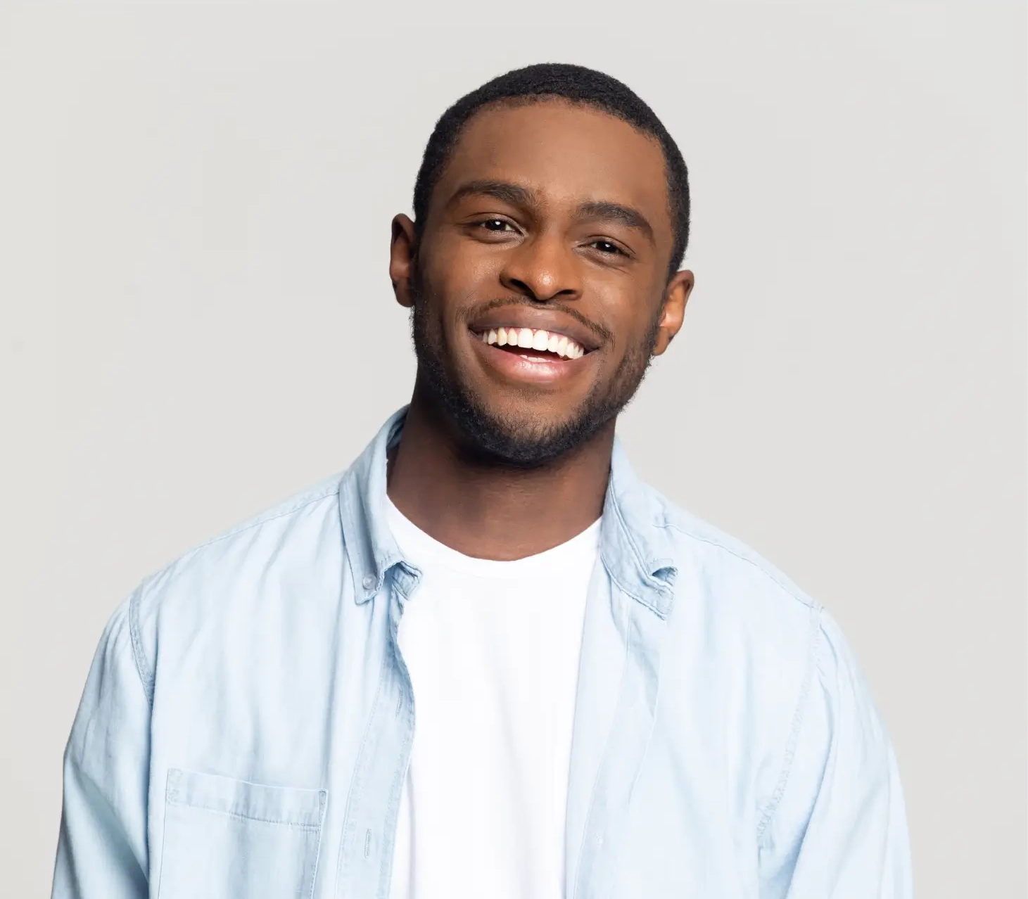 A man in a light blue shirt smiles towards the camera against a plain background.