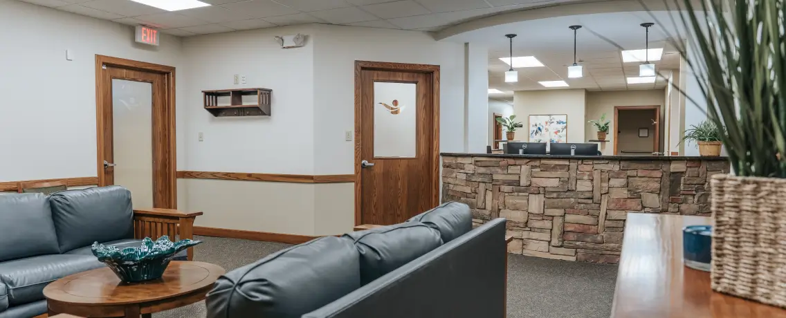 A waiting room with blue couches, a stone-front desk, and potted plants.