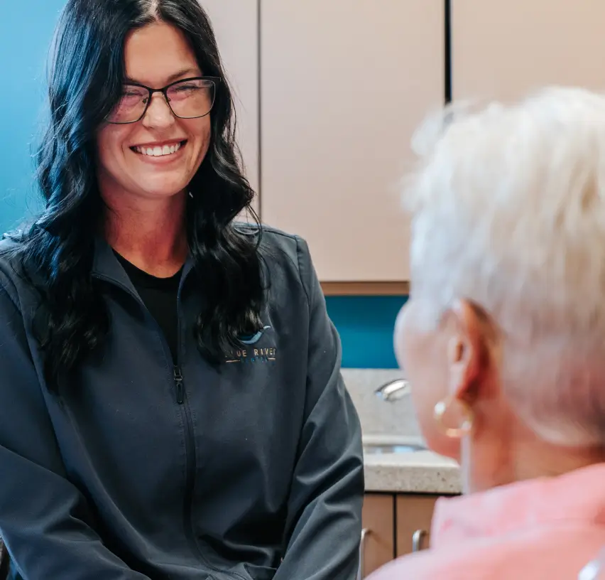 A woman with dark hair smiling and talking to an older woman with short white hair.